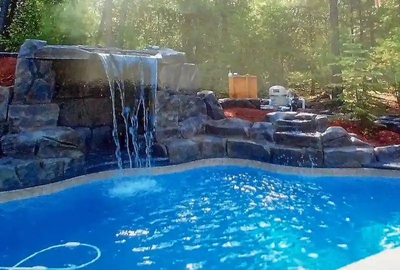 Rock waterfall spilling into a blue pool with trees behind