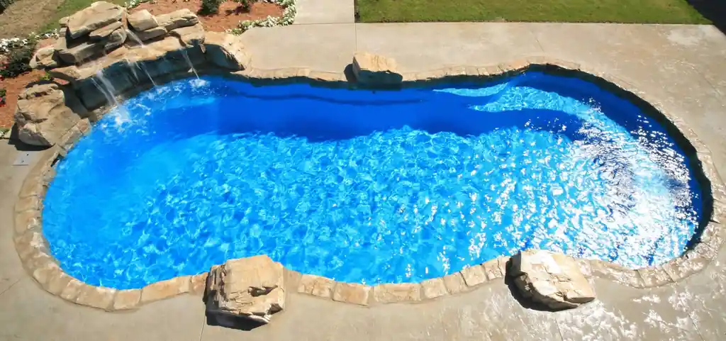 Aerial view of a freeform blue fiberglass pool with a rock waterfall at one end