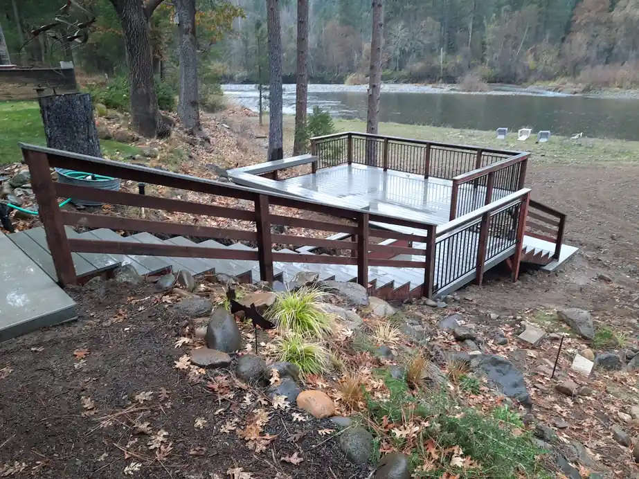 Redwood-railed deck and stairs stepping down a wooded bank toward a river