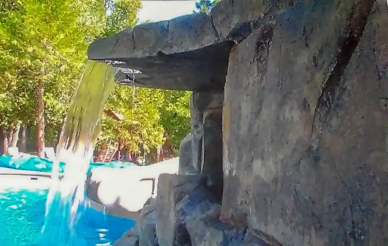 Faux rock waterfall spilling into a pool beside a decorative concrete deck
