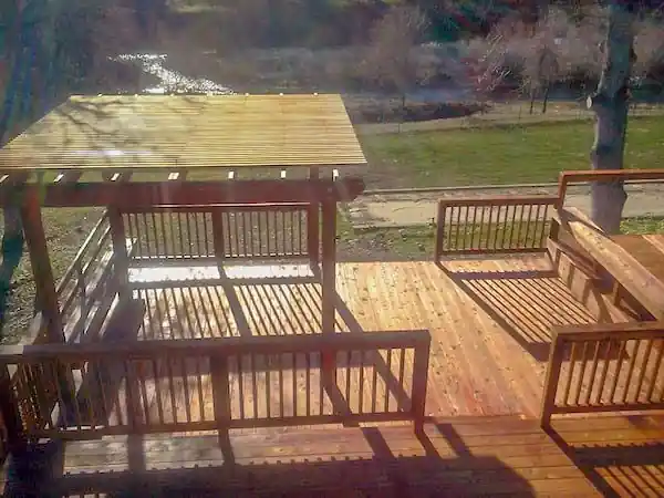 Deck with a pergola, railings and built-in bench seating above a creek