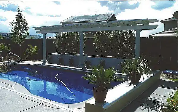 Pool seen through the posts of a pergola, with planting beyond